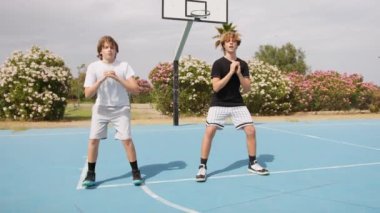 İki genç erkek dışarıda mavi alanda basketbol oynuyorlar..