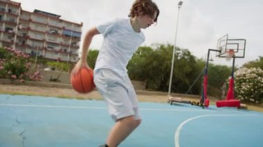 İki genç erkek dışarıda mavi alanda basketbol oynuyorlar..