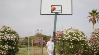 İki genç erkek dışarıda mavi alanda basketbol oynuyorlar..