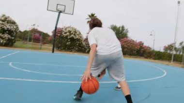 İki genç erkek dışarıda mavi alanda basketbol oynuyorlar..