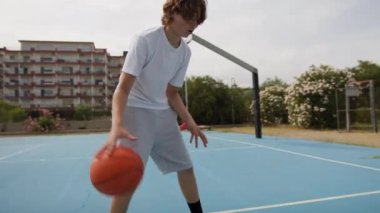 İki genç erkek dışarıda mavi alanda basketbol oynuyorlar..
