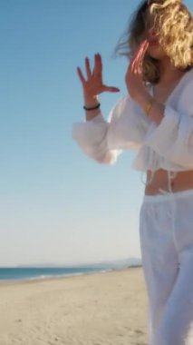 Yazın plajda beyazlar içinde dans eden genç bir kadın.