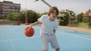 İki genç erkek dışarıda mavi alanda basketbol oynuyorlar..