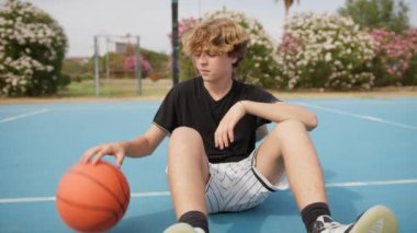 İki genç erkek dışarıda mavi alanda basketbol oynuyorlar..