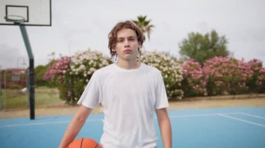 İki genç erkek dışarıda mavi alanda basketbol oynuyorlar..