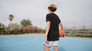 İki genç erkek dışarıda mavi alanda basketbol oynuyorlar..