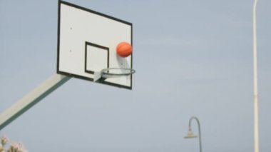 İki genç erkek dışarıda mavi alanda basketbol oynuyorlar..