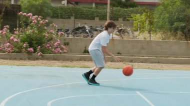 İki genç erkek dışarıda mavi alanda basketbol oynuyorlar..