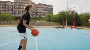 İki genç erkek dışarıda mavi alanda basketbol oynuyorlar..