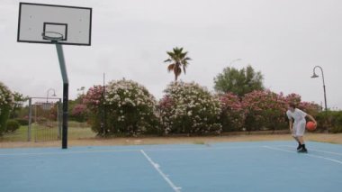 İki genç erkek dışarıda mavi alanda basketbol oynuyorlar..