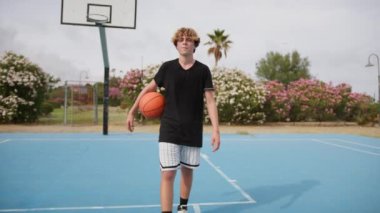 İki genç erkek dışarıda mavi alanda basketbol oynuyorlar..