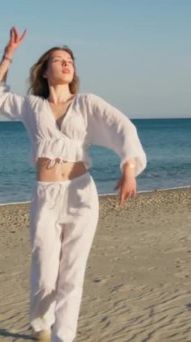 Yazın plajda beyazlar içinde dans eden genç bir kadın.