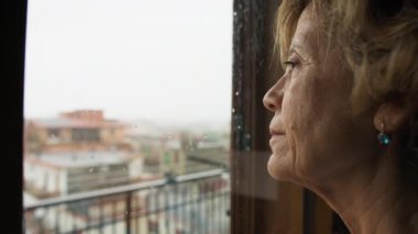 Kadın evdeki pencereden yağmuru endişeli bir şekilde izliyor..