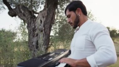 Beyaz gömlekli çocuk dışarıdaki doğada piyano çalıyor..