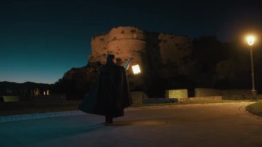 Gizemli genç kadın pelerin ve fenerle bir köyün sokaklarında yürüyor..