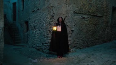 Gizemli genç kadın pelerin ve fenerle bir köyün sokaklarında yürüyor..