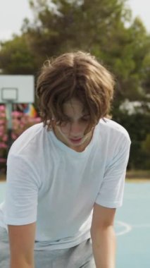 İki genç erkek dışarıda mavi alanda basketbol oynuyorlar..