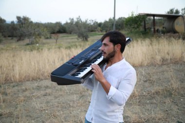 Beyaz gömlekli çocuk dışarıdaki doğada piyano çalıyor..