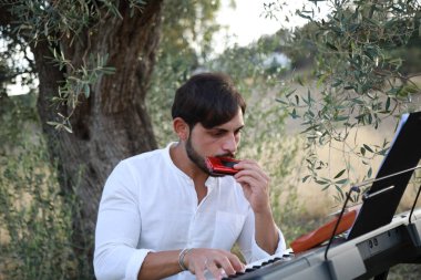 Beyaz gömlekli çocuk dışarıdaki doğada piyano çalıyor..