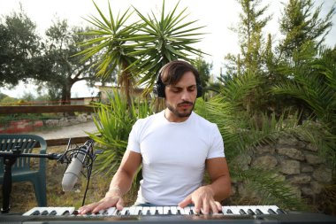 Beyaz gömlekli çocuk dışarıdaki doğada piyano çalıyor..