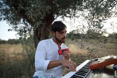 Beyaz gömlekli çocuk dışarıdaki doğada piyano çalıyor..