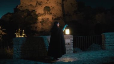 Gizemli genç kadın pelerin ve fenerle bir köyün sokaklarında yürüyor..