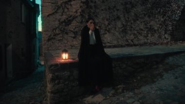 Gizemli genç kadın pelerin ve fenerle bir köyün sokaklarında yürüyor..