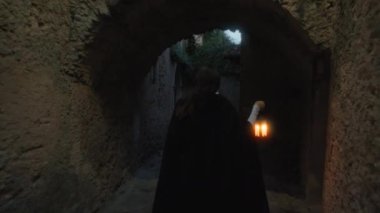 Gizemli genç kadın pelerin ve fenerle bir köyün sokaklarında yürüyor..
