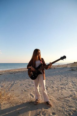 Sahilin yanındaki doğada bas gitar çalan bir kız..