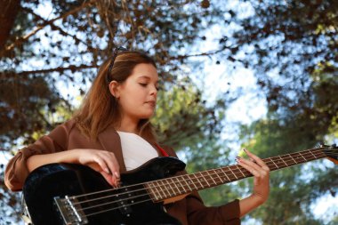 Sahilin yanındaki doğada bas gitar çalan bir kız..