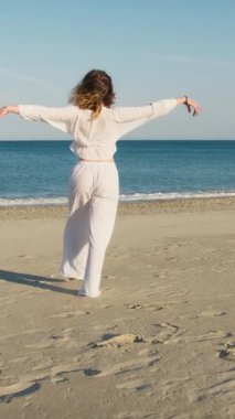 Yazın plajda beyazlar içinde dans eden genç bir kadın.