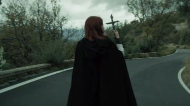 Bulutlu bir günde kırsalda pelerinli genç bir kadın..