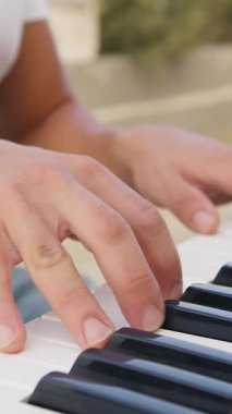 Beyaz gömlekli çocuk dışarıdaki doğada piyano çalıyor..