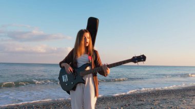 Sahilin yanındaki doğada bas gitar çalan bir kız..