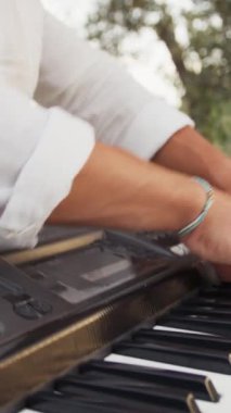 Beyaz gömlekli çocuk dışarıda klavye çalıyor..