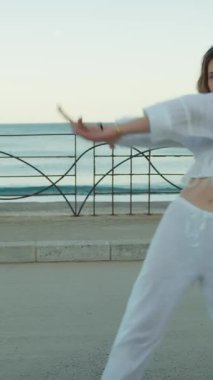 Yazın plajda beyazlar içinde dans eden genç bir kadın.