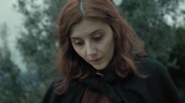 Bulutlu bir günde kırsalda pelerinli genç bir kadın..