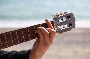 Adam yazın deniz kenarındaki sahilde klasik gitar çalıyor..