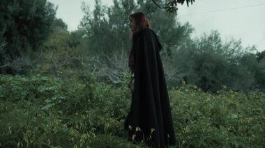 Bulutlu bir günde kırsalda pelerinli genç bir kadın..