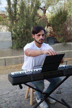 Beyaz gömlekli çocuk dışarıdaki doğada piyano çalıyor..