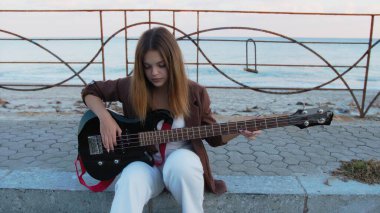 Sahilin yanındaki doğada bas gitar çalan bir kız..