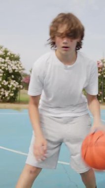 İki genç erkek dışarıda mavi alanda basketbol oynuyorlar..