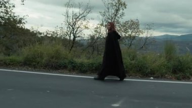 Bulutlu bir günde kırsalda pelerinli genç bir kadın..