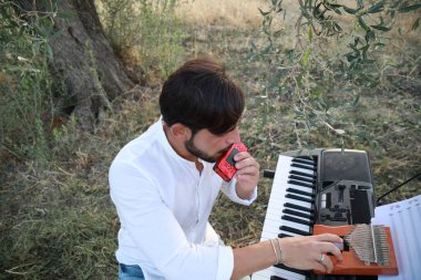 Beyaz gömlekli çocuk dışarıdaki doğada piyano çalıyor..