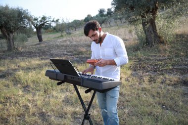 Beyaz gömlekli çocuk dışarıdaki doğada piyano çalıyor..