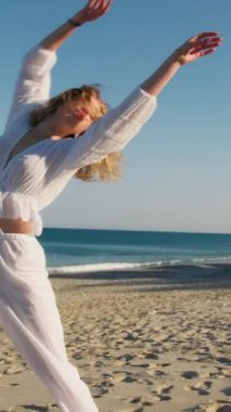 Yazın plajda beyazlar içinde dans eden genç bir kadın.