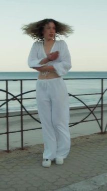 Yazın plajda beyazlar içinde dans eden genç bir kadın.