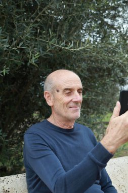 Yaşlı adam kırsal kesimde görüntülü arama yapıyor ve telefonla konuşuyor..