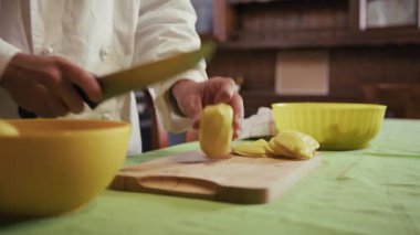 Bir çırak şefin elleri mutfaktaki kesme tahtasına patatesleri kesiyor..