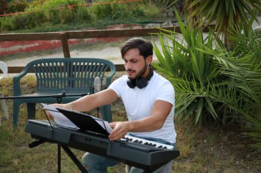 Beyaz gömlekli çocuk dışarıdaki doğada piyano çalıyor..